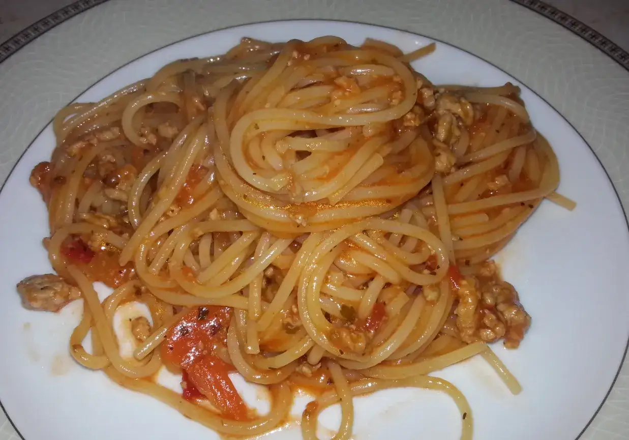 Pyszne spaghetti bolognese z passaty, z mielonym mięsem i kawałkami pomidorów, podane na białym talerzu.