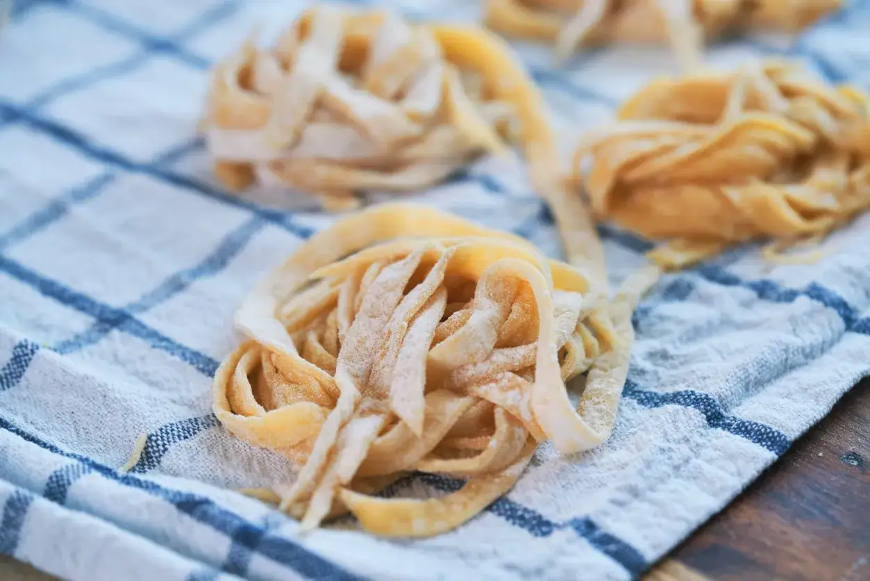 Świeże, domowe tagliatelle lub makaron spaghetti ułożone na lnianym ręczniku w kratkę.