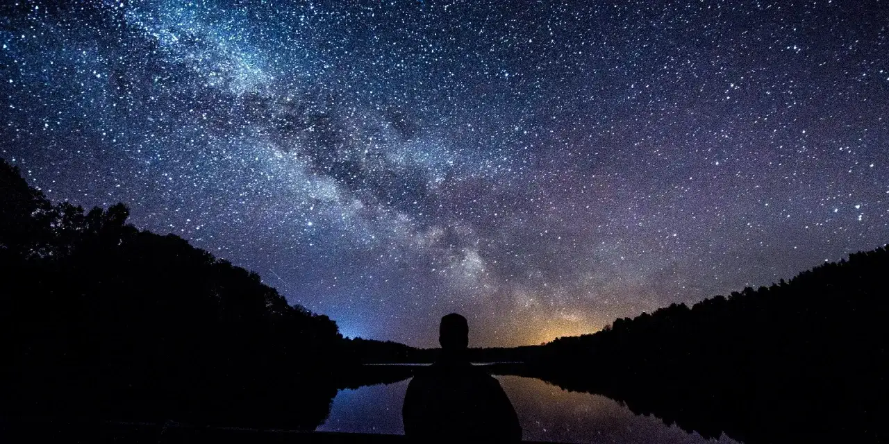 Zachwycająca fotografia astronomiczna Drogi Mlecznej nad jeziorem. Sylwetka człowieka kontempluje kosmos.