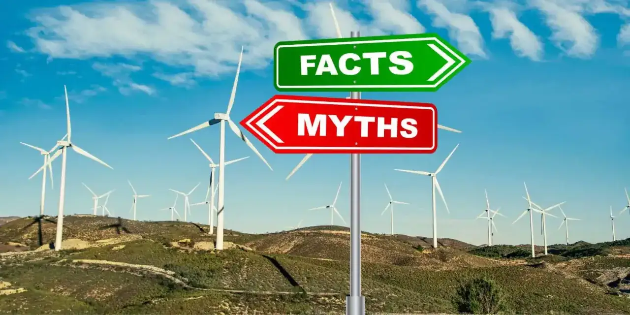 Znak drogowy "Fakty" i "Mity" na tle farmy wiatrowej. Czy wiatraki są szkodliwe? Sprawdź fakty, nie mity.