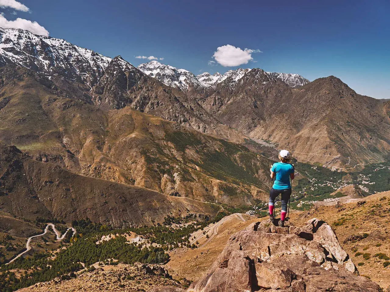 Widok na ośnieżone szczyty górskie Jebel Toubkal. Turystka podziwia panoramę z skalistego zbocza.