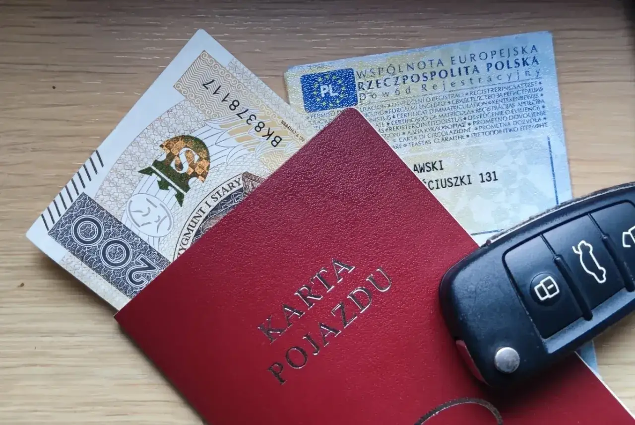 Karta pojazdu, dowód rejestracyjny, pieniądze i kluczyki samochodowe na drewnianym tle.