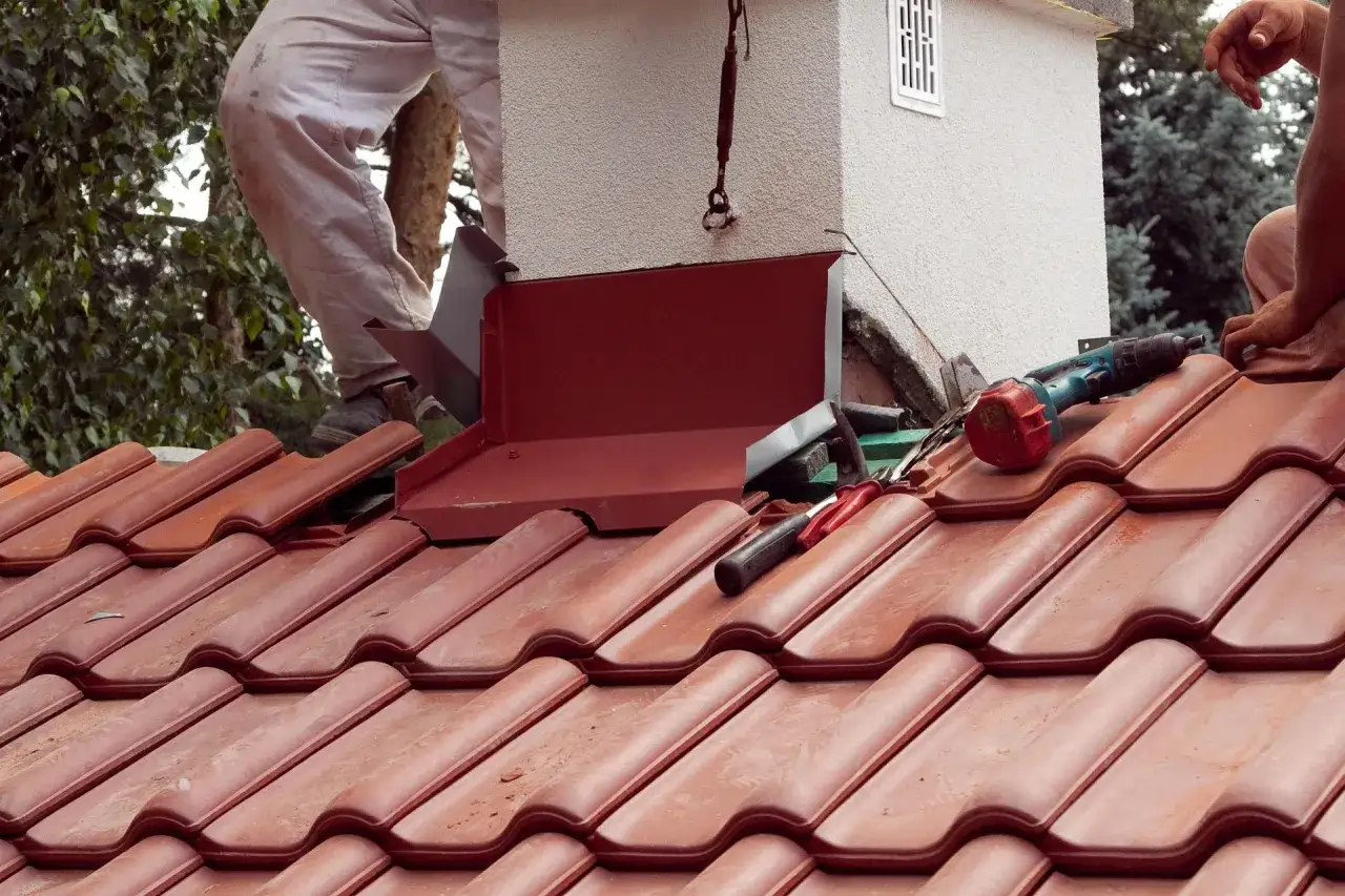 Prace dekarskie przy kominie: montaż obróbki blacharskiej na dachu z dachówki.