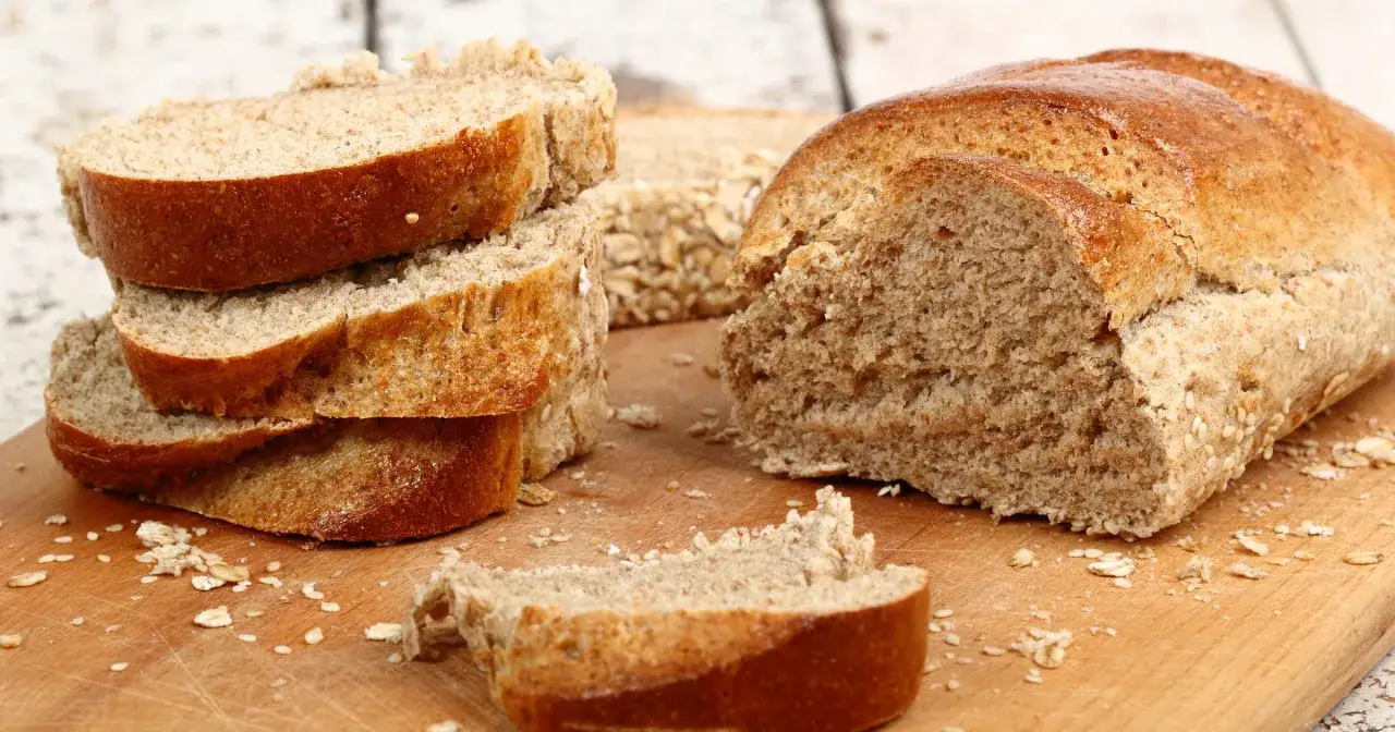 Krojony chleb graham na desce, posypany płatkami owsianymi. Czy chleb graham jest dietetyczny? Tak, to świetny wybór dla dbających o linię.