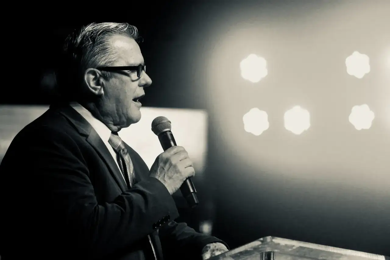 Mężczyzna w garniturze przemawia do mikrofonu. Jego motywacja do pracy płynie z chęci dzielenia się wiedzą i inspirowania innych.