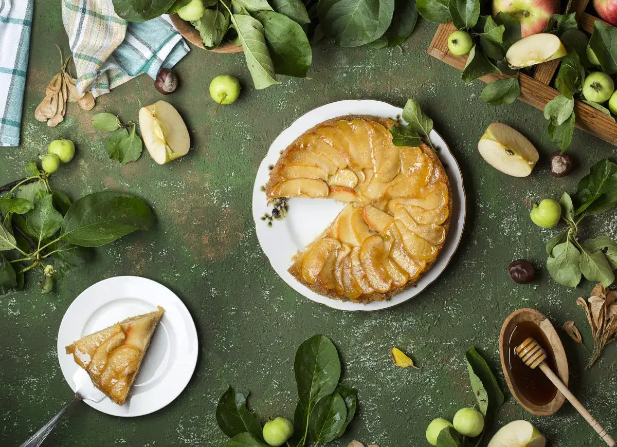 Szarlotka i jabłecznik na zielonym tle, otoczone jabłkami i liśćmi.