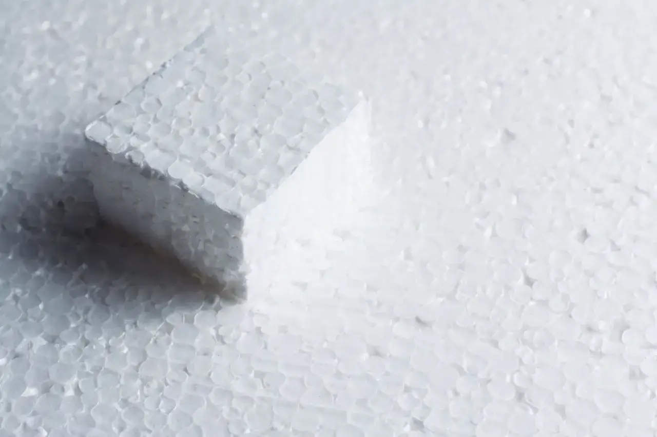 Kostka styropianu na tle drobnych kuleczek styropianu.