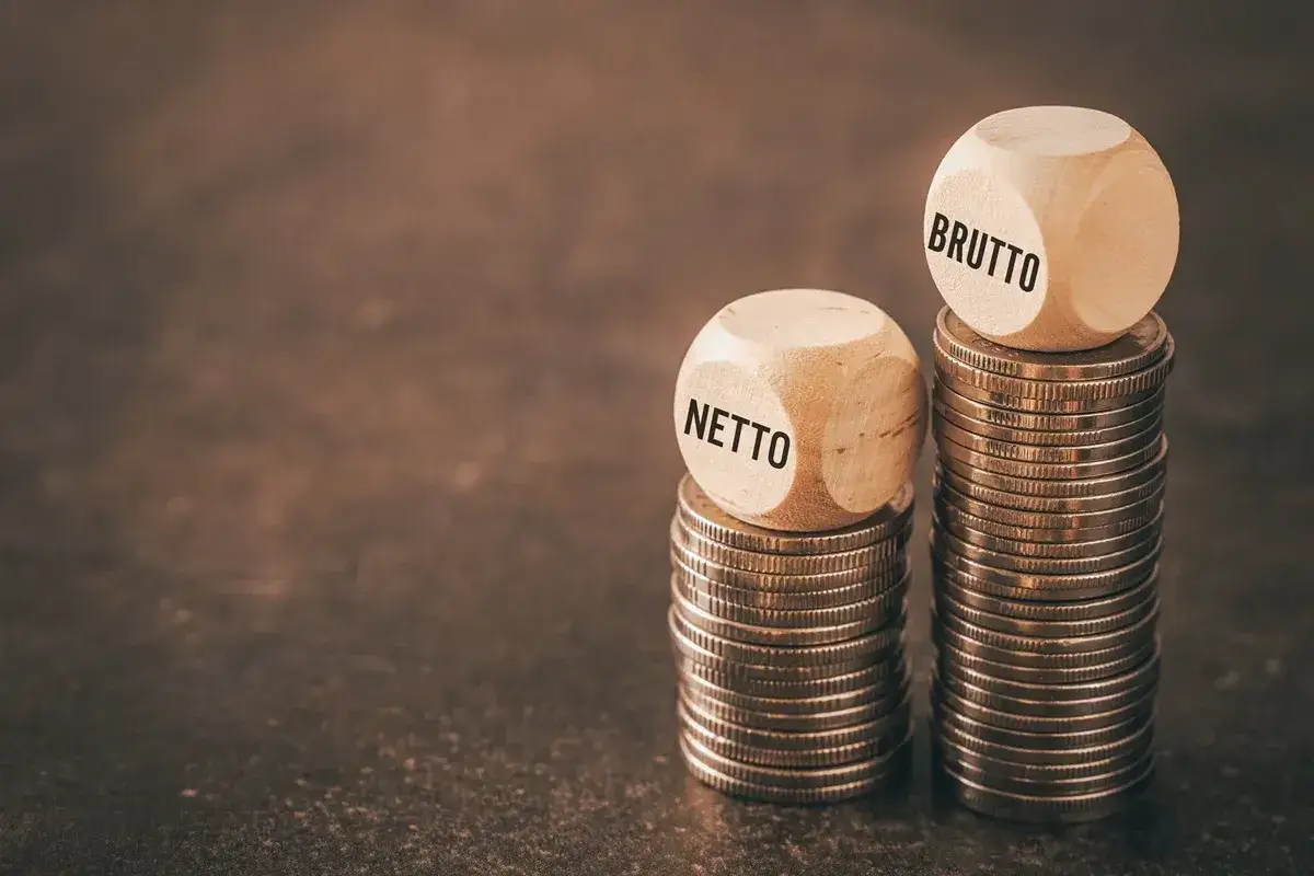 Dwie stosy monet, na jednej kostka z napisem "NETTO", na drugiej z napisem "BRUTTO".