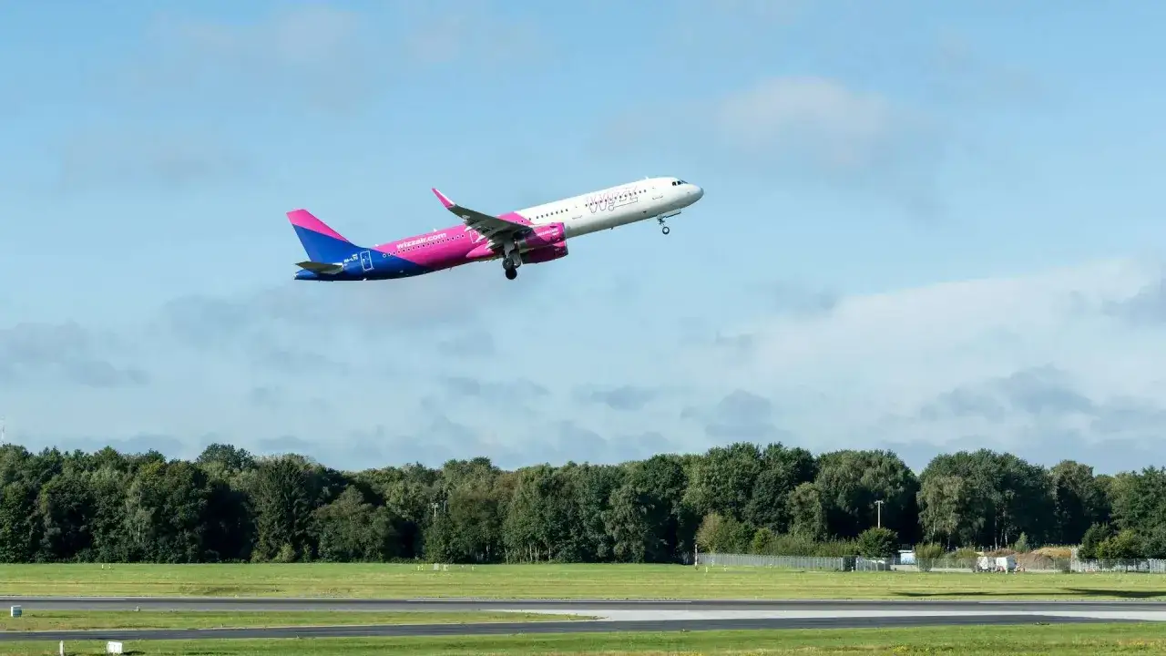 Samolot Wizz Air wznosi się na tle błękitnego nieba z chmurami.