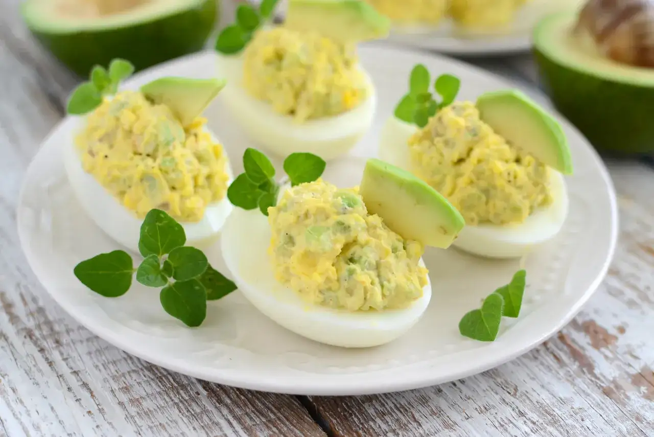 Pyszne jajka faszerowane awokado, udekorowane plasterkami awokado i świeżymi ziołami. Idealna przekąska.