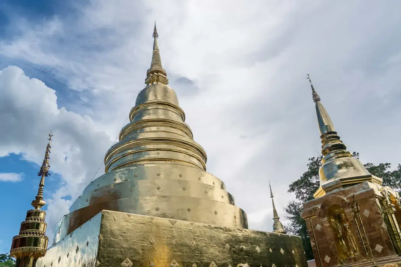 Złote stupy świątyni Wat Phra Singh w Chiang Mai na tle błękitnego nieba z chmurami.