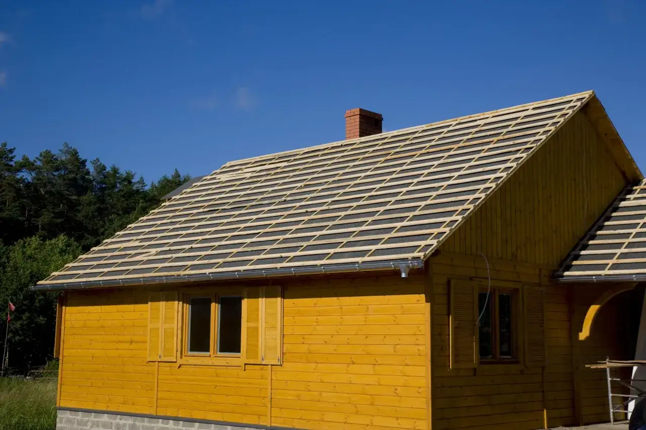 Dach drewnianego domu w budowie, przygotowany pod deskowanie pod blachodachówkę. Widać rusztowanie i komin.