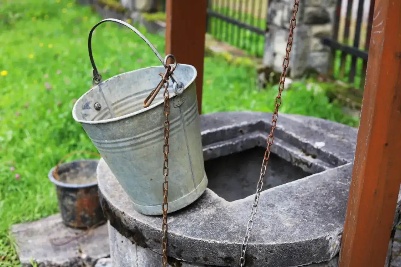 Metalowy wiaderko przy studni, gotowe do pracy. Ktoś zastanawia się, jak wykopać studnię, by mieć własne źródło wody.