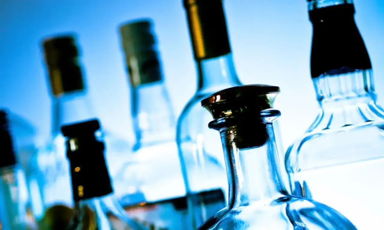 Kilka szklanych butelek alkoholu na niebieskim tle.