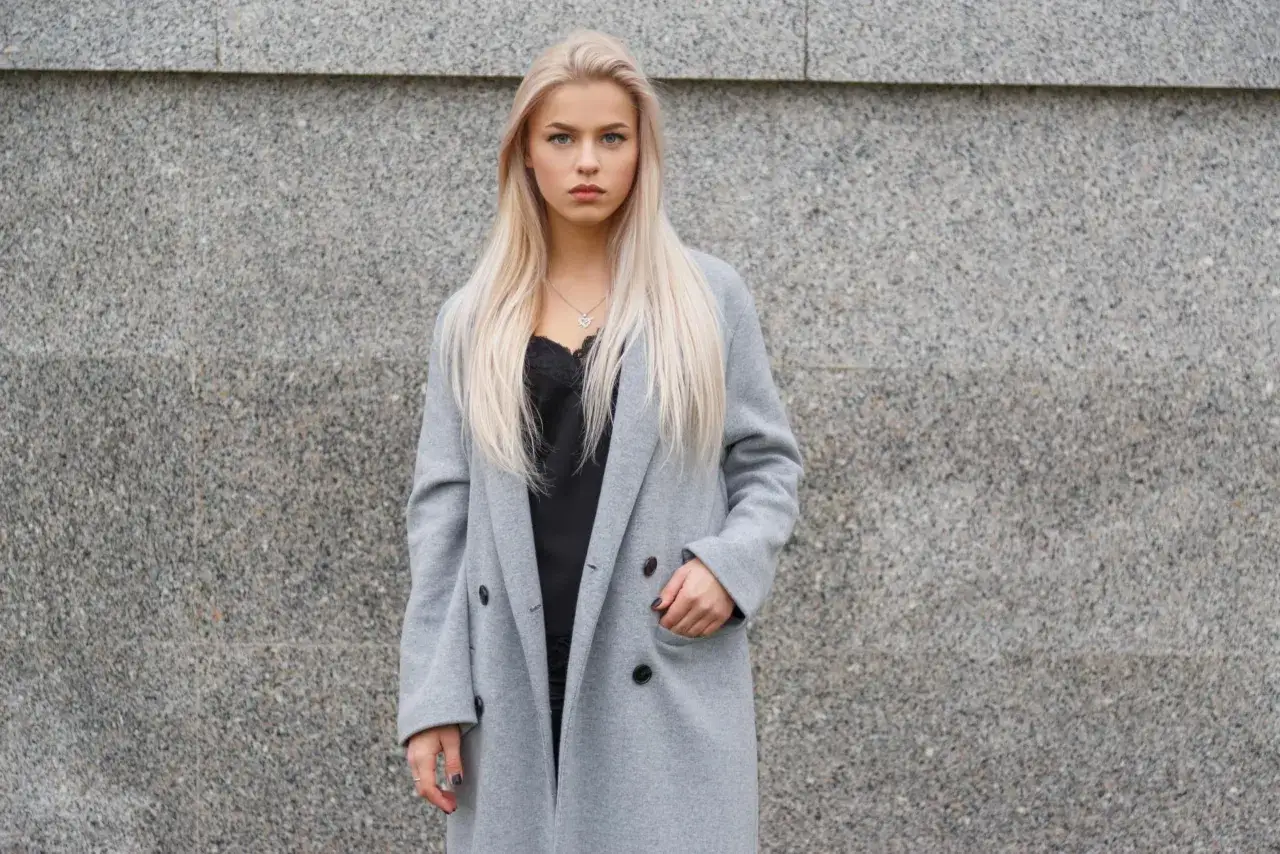 Blondynka w szarym płaszczu i czarnej koronkowej bluzce. Czerń to klasyczny wybór, jaki kolor pasuje do szarego ubrania, dodając elegancji.