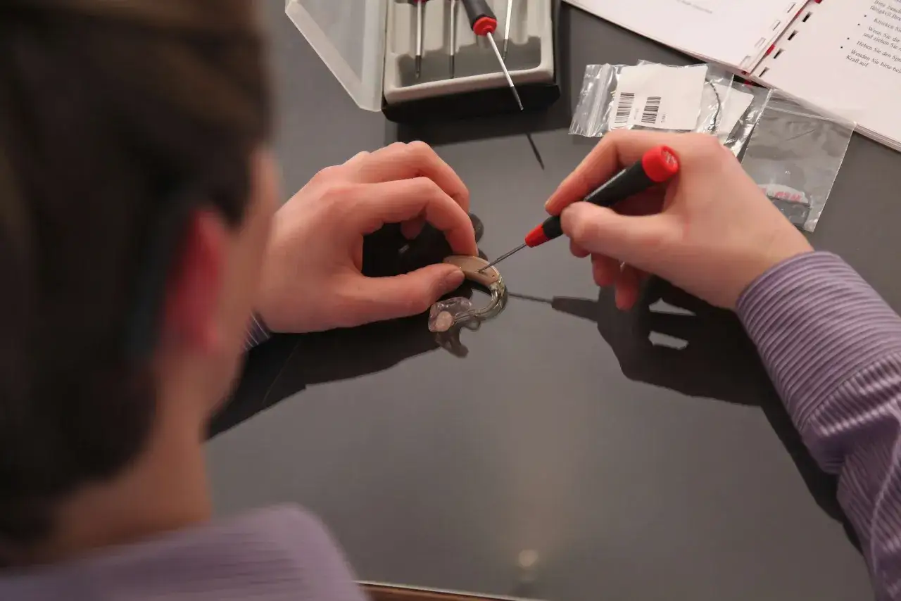 Ręce majstrują przy aparacie słuchowym, by go naprawić. Instrukcja podpowiada, jak znaleźć zgubiony aparat słuchowy, gdyby się zawieruszył.