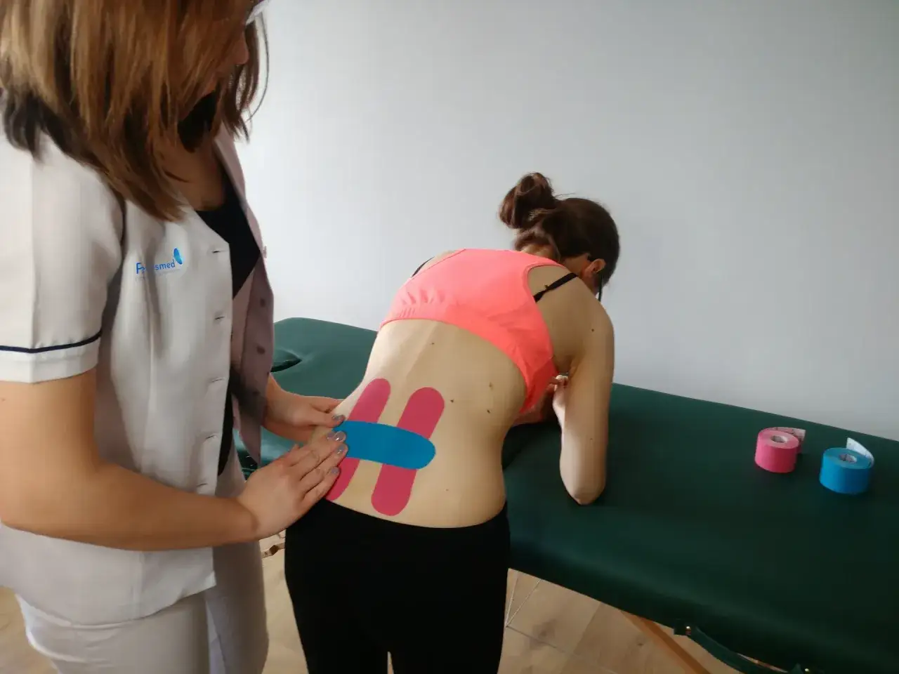 Fizjoterapeuta aplikuje taśmy kinezjotaping na plecy pacjentki po cesarskim cięciu.