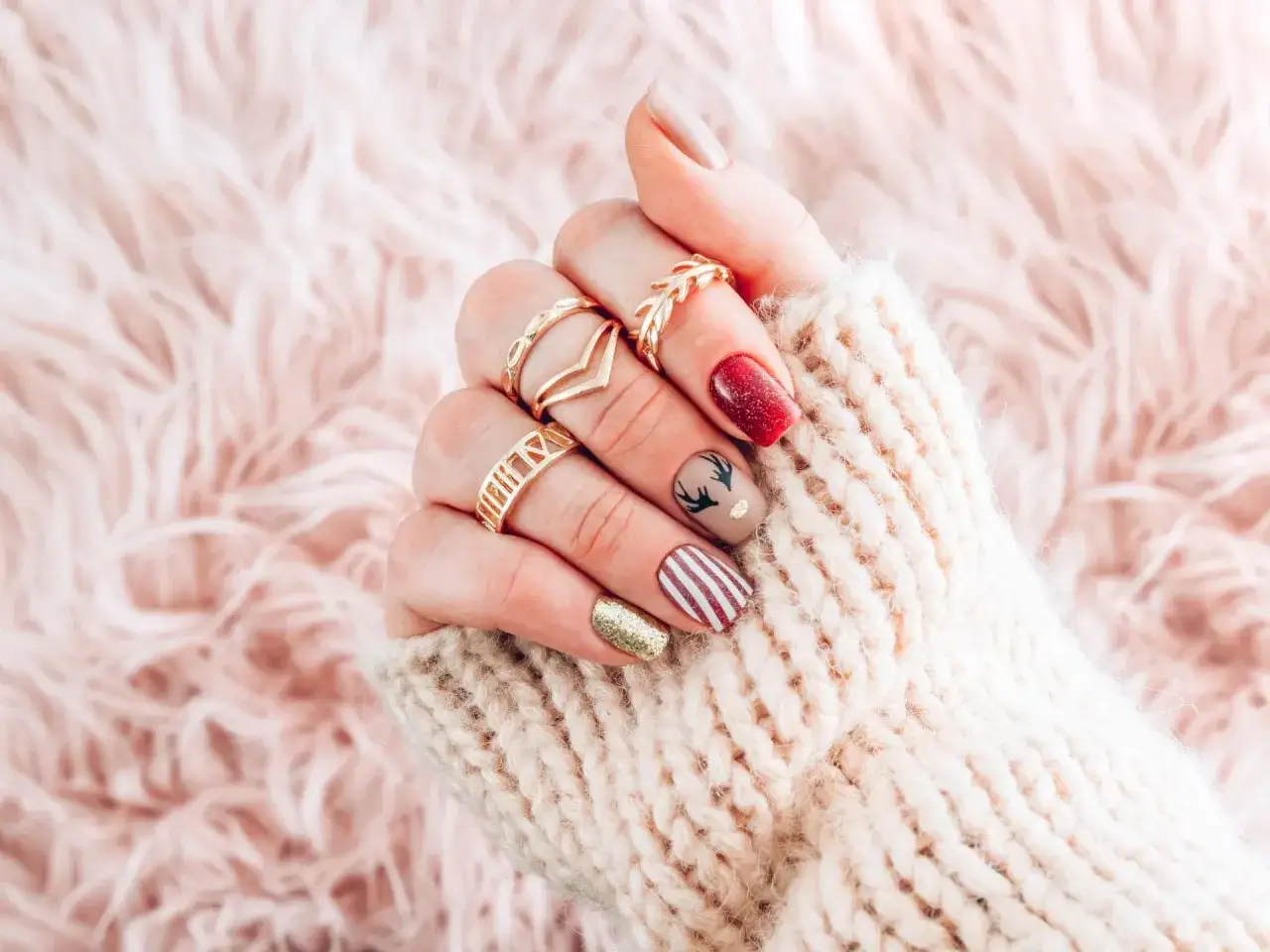 Festliche nägel zu weihnachten mit Rentier-Motiv, roten und goldenen Akzenten, umgeben von einem kuscheligen Strickpullover.