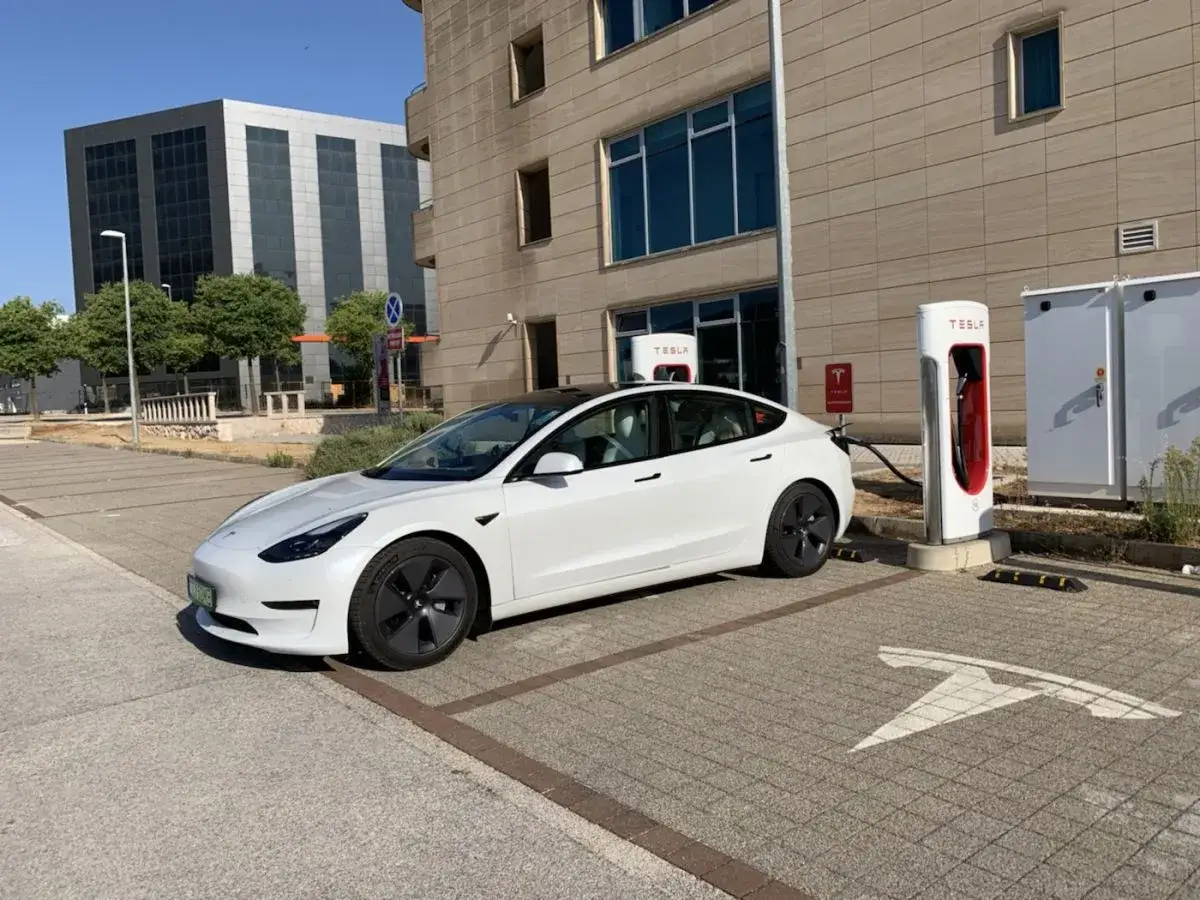 Biały Tesla Model 3, zasilany energią, czeka na ładowanie. Zastanawiasz się, ile koni ma ten model?