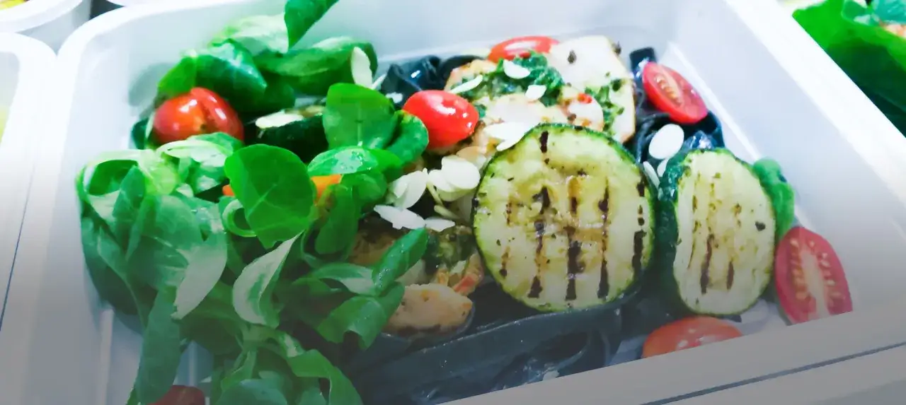 Kolorowy catering dietetyczny z grillowaną cukinią, pomidorkami i zielonymi liśćmi. Dowiedz się, jak podgrzewać catering dietetyczny, by zachować świeżość.