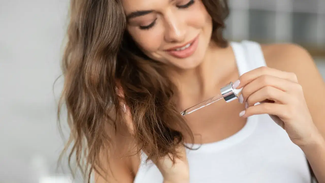 Uśmiechnięta kobieta aplikuje olejek na swoje falowane włosy. Dowiedz się, jak olejować włosy wysokoporowate dla ich zdrowia i blasku.