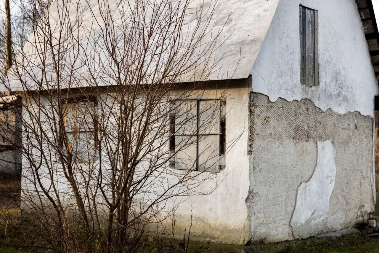 Elewacje starych domów: zniszczony tynk, puste okna i nagie gałęzie drzew tworzą melancholijną galerię.