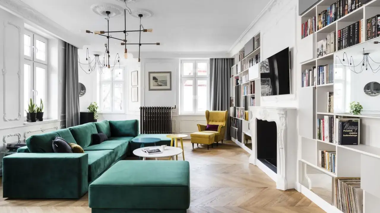 Elegancki salon w stylu paryskim z zieloną kanapą, żółtym fotelem i regałami pełnymi książek.