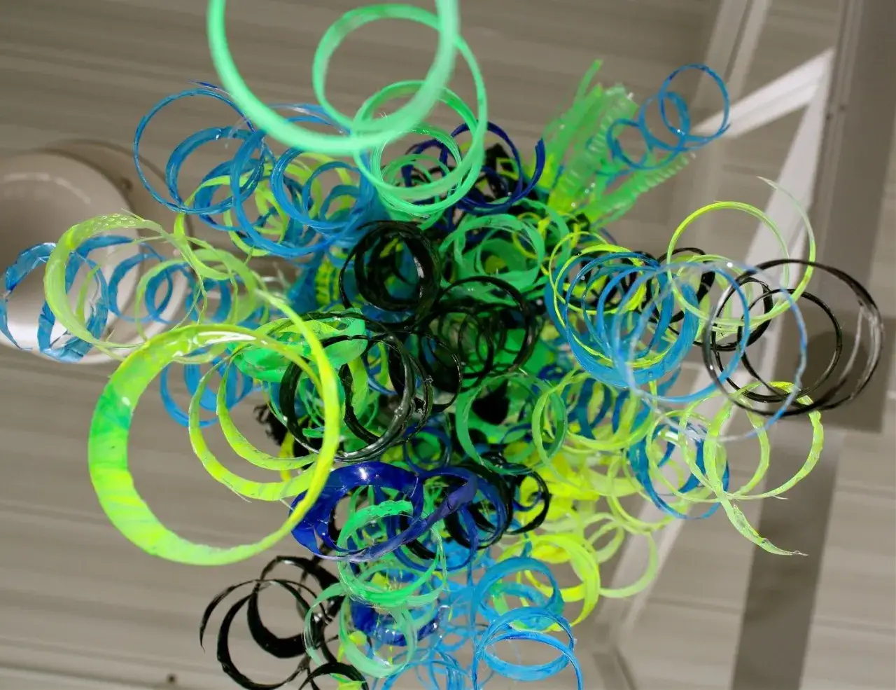 Kolorowa instalacja z upcyklingowanych plastikowych pierścieni w odcieniach zieleni, niebieskiego i czarnego.