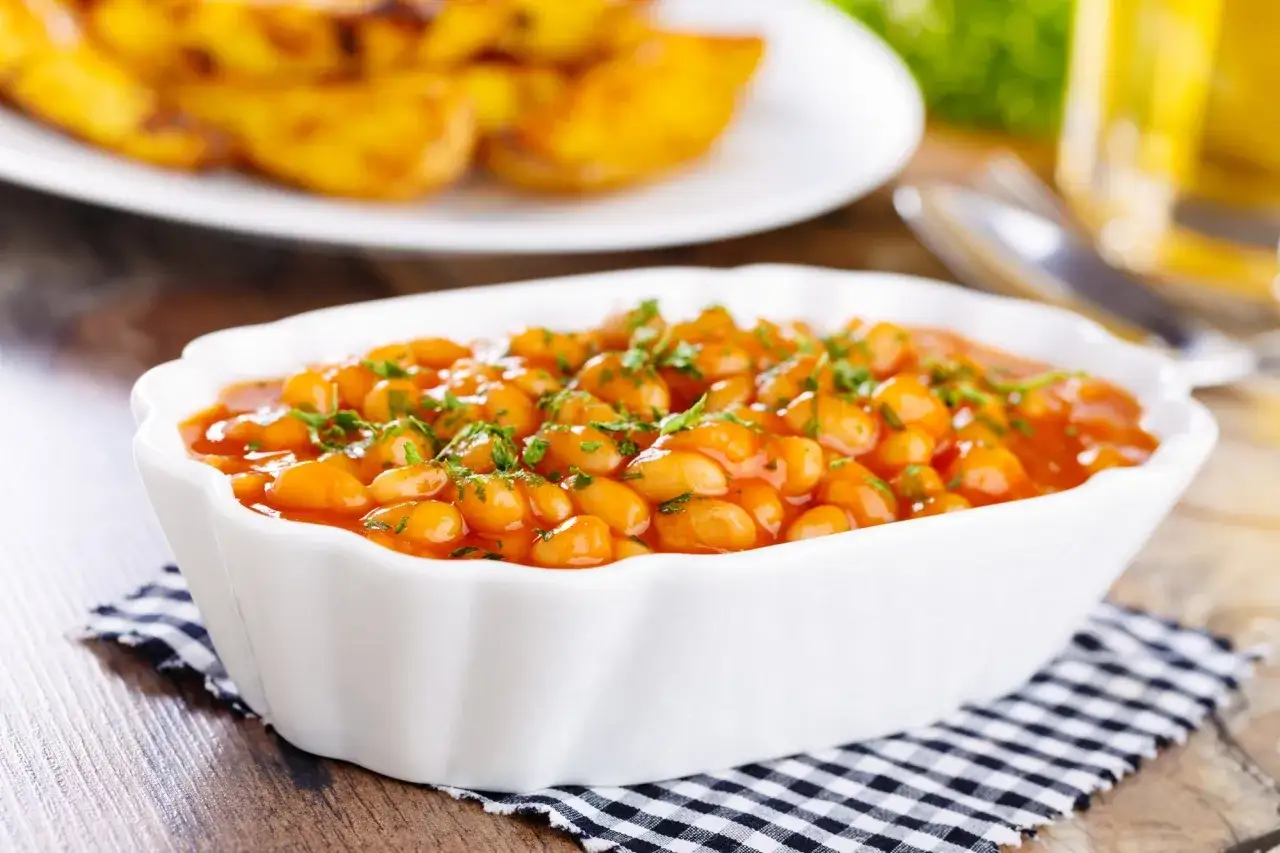 Aksamitna fasolka po bretońsku w sosie pomidorowym, posypana natką pietruszki. Obok talerz pieczonych ziemniaków.