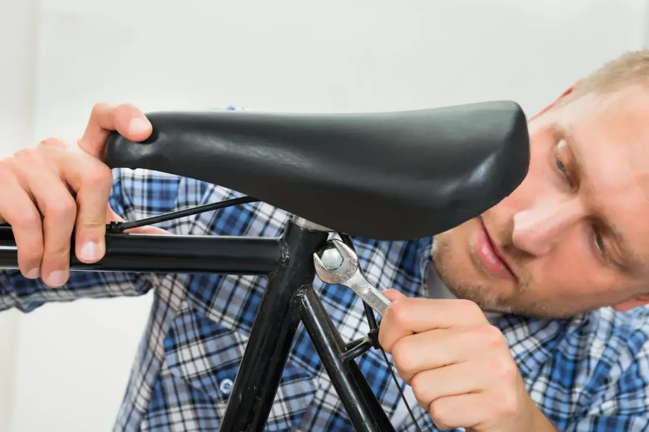 Mężczyzna w kratę reguluje kluczem siodełko roweru MTB.