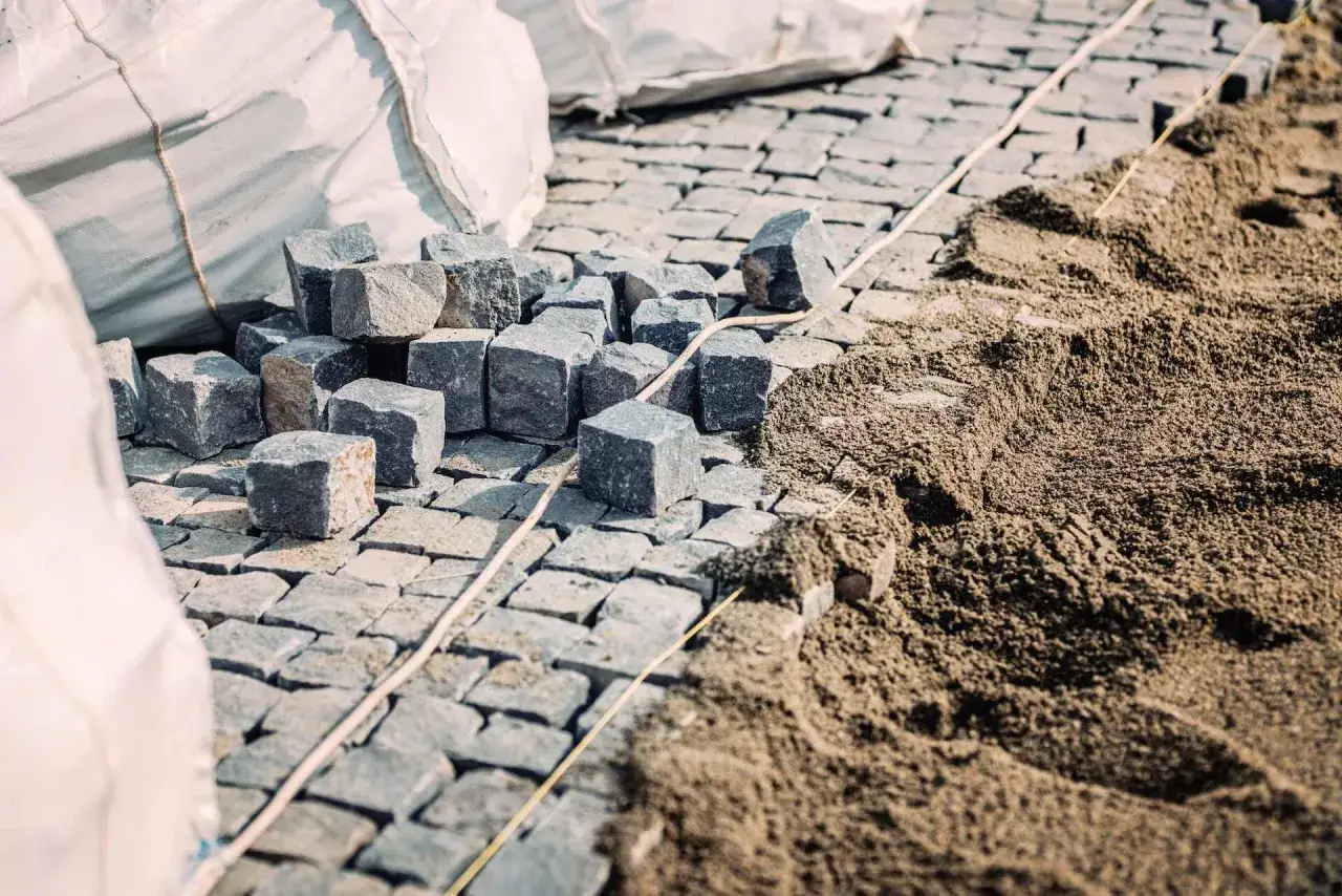 Kupa kostki brukowej i piasku, gotowe do ułożenia. Widać worki z materiałem i przygotowany podkład, czyli ile podsypki pod kostkę potrzeba.