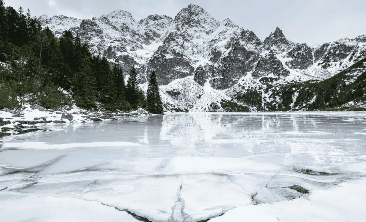 Mroźna tafla jeziora i ośnieżone szczyty Tatr. Bukowina Tatrzańska co warto zobaczyć? To zimowe cuda natury!