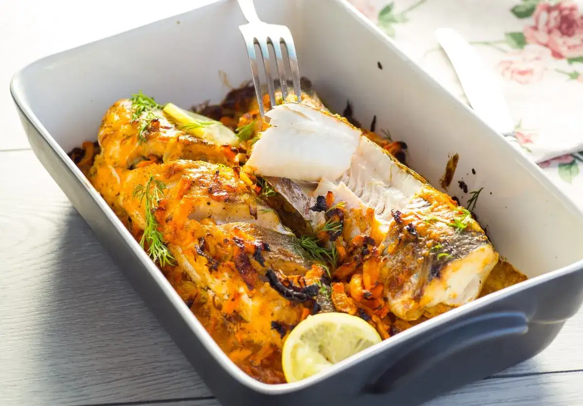 Pieczony dorsz z warzywami i cytryną w naczyniu żaroodpornym.