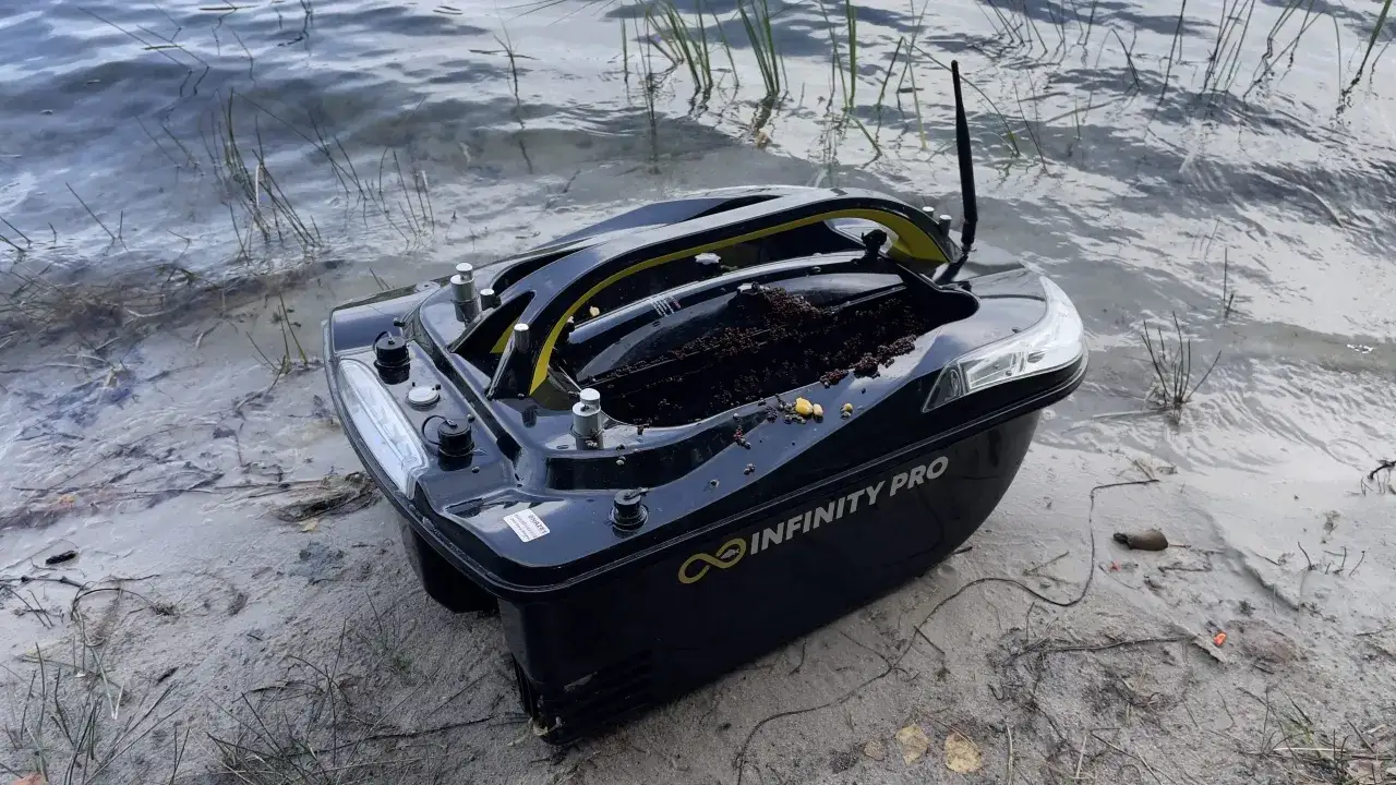 Czarna łódka do zanęty "Infinity Pro" z anteną, gotowa do wypłynięcia na spokojne wody.