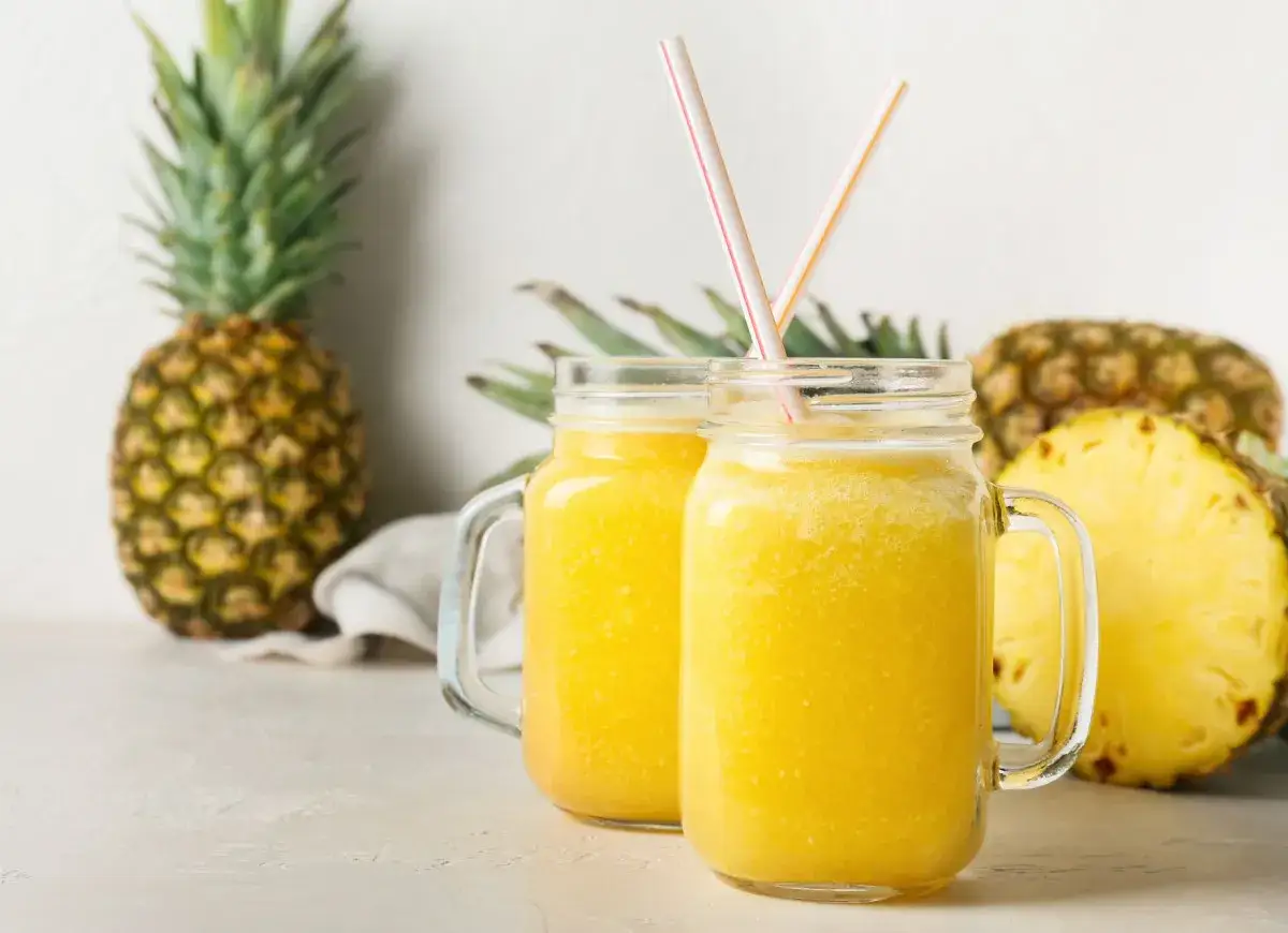 Orzeźwiający drink w ananasie, podany w słoikach, z kawałkami ananasa w tle.