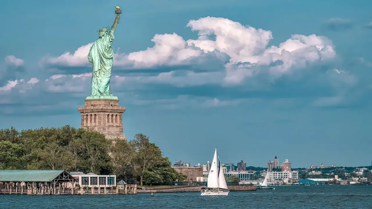 Statua Wolności i żaglówka na wodzie. Zastanawiasz się, ile kosztuje lot do USA z Polski?