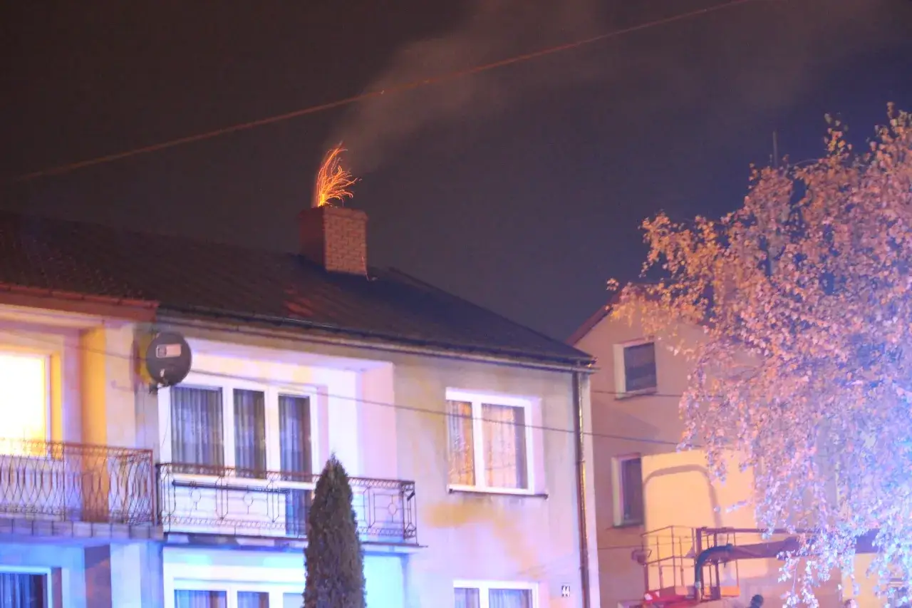 Jasny komin z cegły, z którego lecą iskry, sugeruje, dlaczego lecą iskry z komina. W tle widać dom i drzewo.
