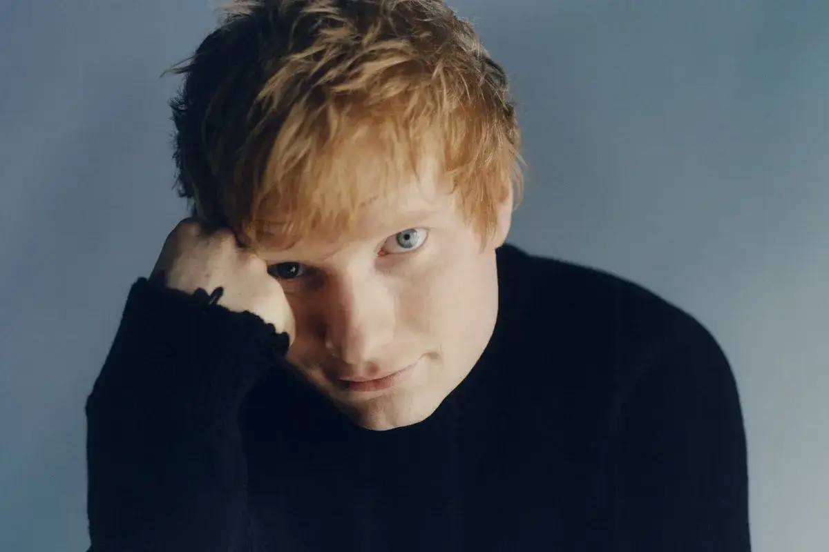 Ed Sheeran w czarnym golfie, opierający głowę na dłoni.