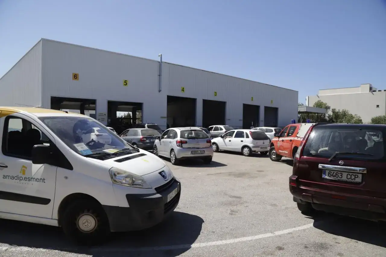 Furgoneta blanca y varios coches aparcados frente a un edificio con puertas de garaje numeradas.