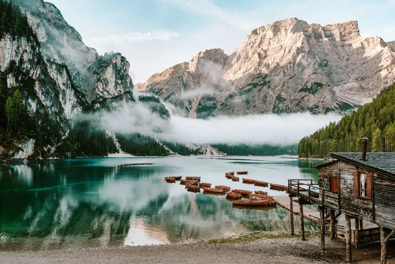 Spokojne jezioro w Dolomitach, Tyrol Włochy, z łodziami przy drewnianym molo i mgłą otulającą góry.