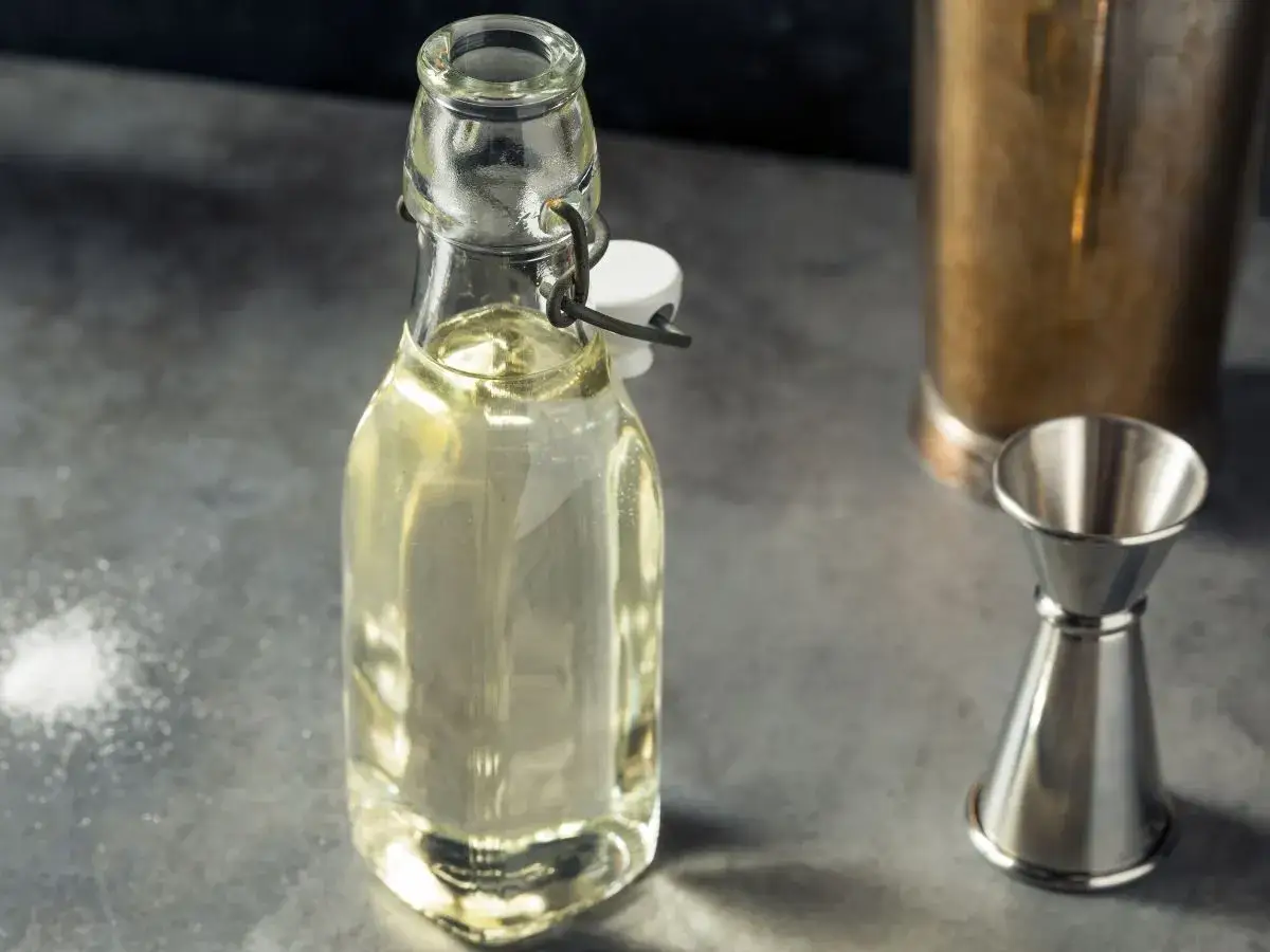 Domowy syrop cukrowy (simple syrup) w butelce, obok jigger i shakera. Idealny do drinków, łatwy do przygotowania krok po kroku.