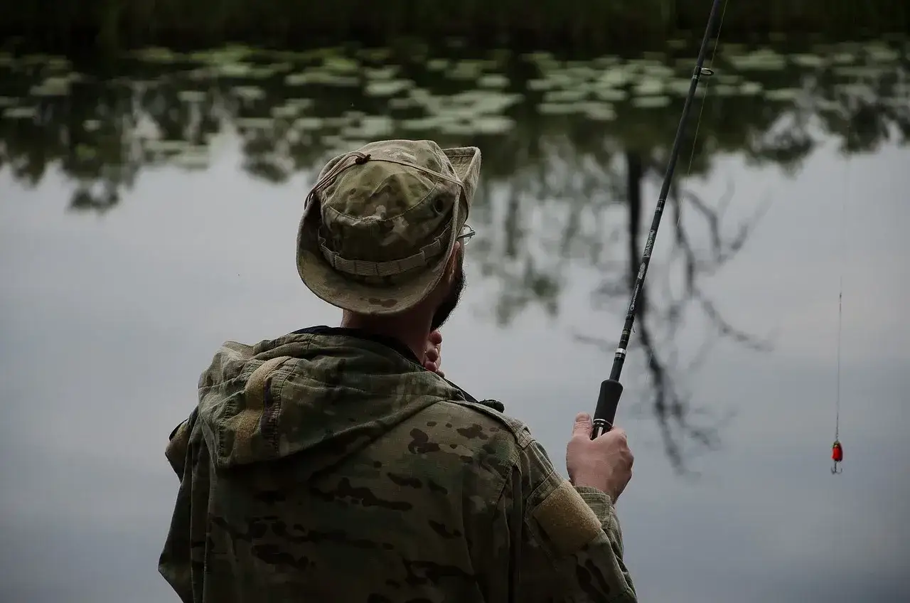 Wędkarz w kamuflażu przygotowuje się do łowienia. Pokazano, jak uzbroić wędkę na spinning, z przynętą gotową do zarzucenia.