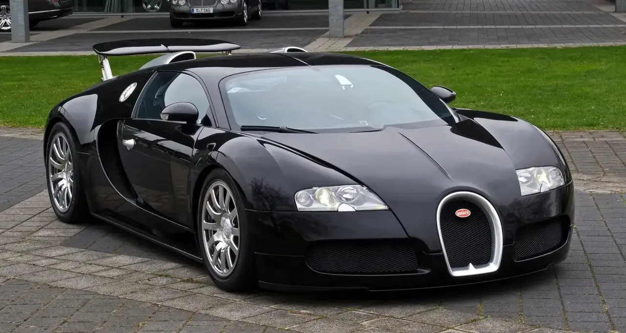 Czarny Bugatti Veyron z dużym tylnym spojlerem zaparkowany na bruku.
