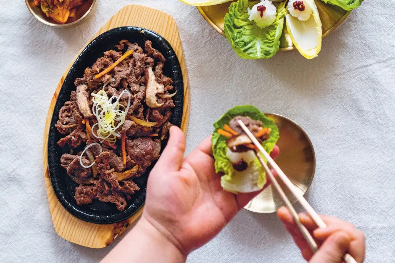 Pyszne bulgogi przepis na talerzu. Ktoś właśnie przygotowuje idealny kęs w liściu sałaty.