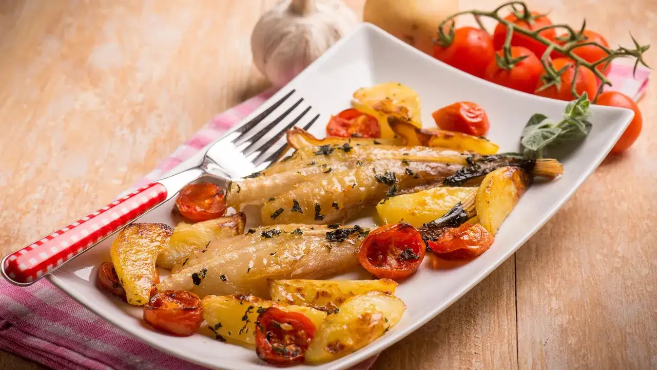 Pieczony mintaj z ziemniakami i pomidorkami koktajlowymi na białym talerzu.