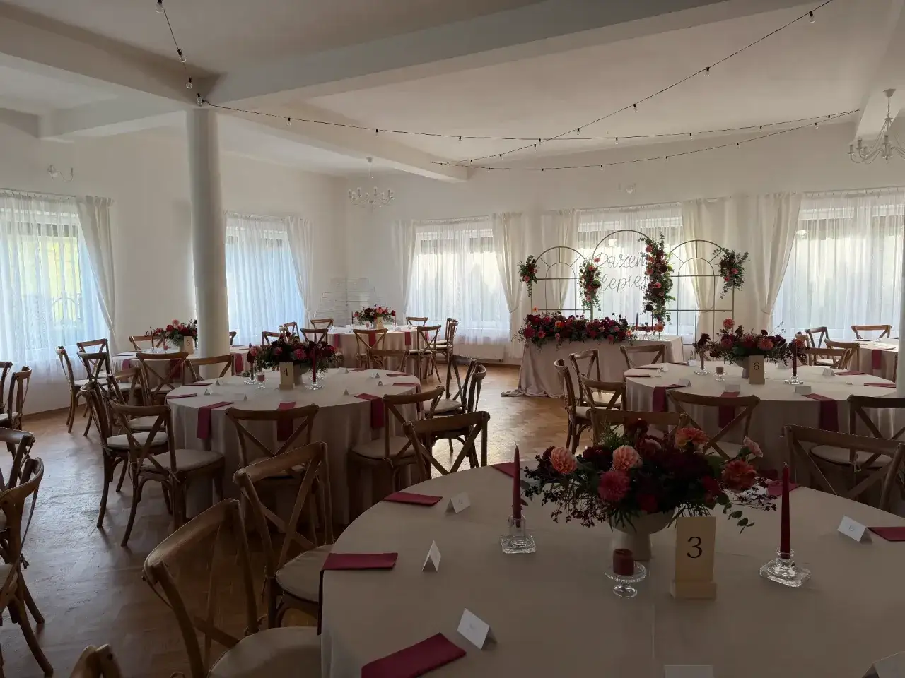 Elegancka sala weselna z okrągłymi stołami, kwiatami i świecami. Idealne miejsce, by wybrać najlepszą salę na wesele.