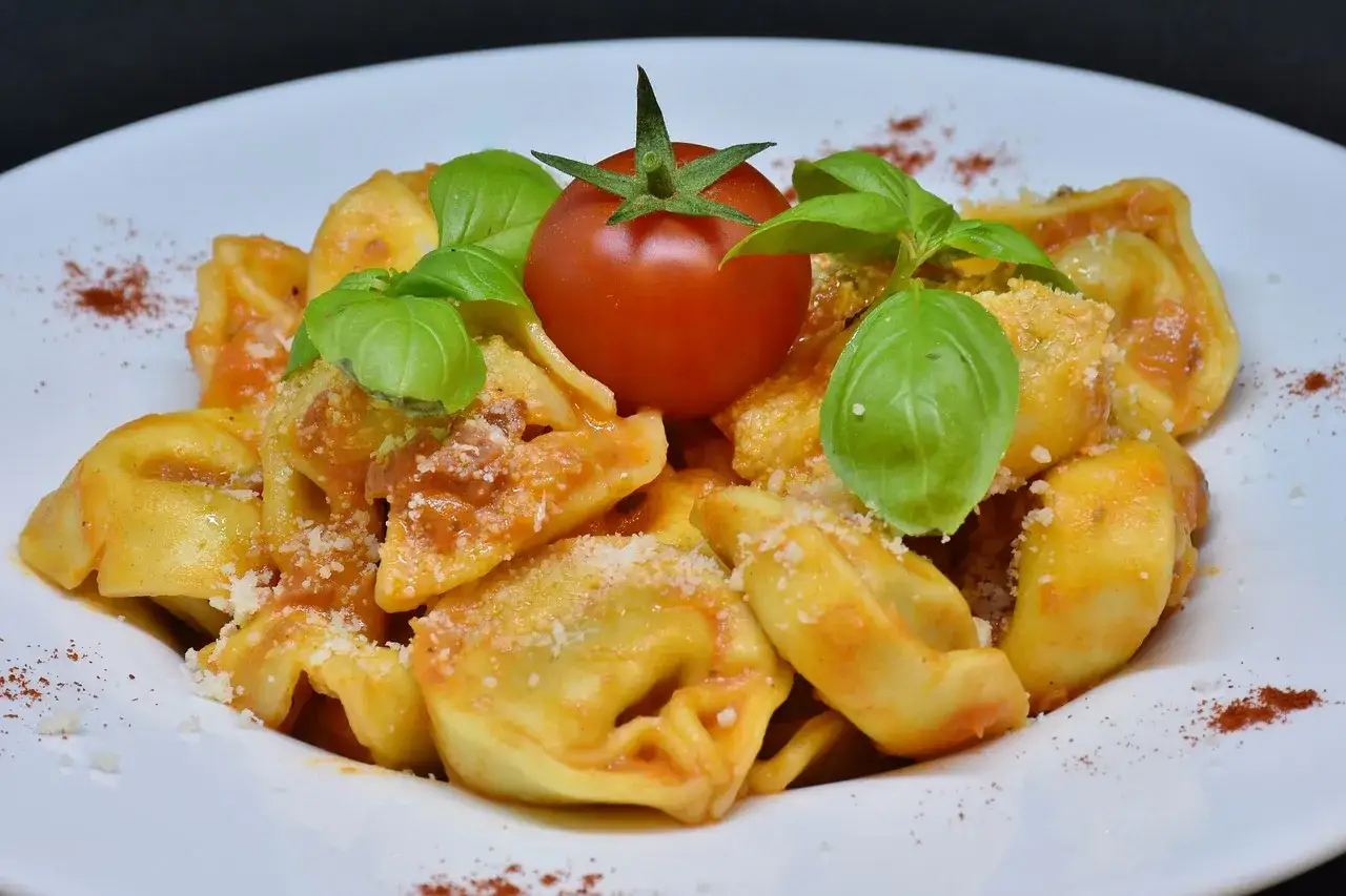 Tortellini z sosem pomidorowym, posypane parmezanem, udekorowane pomidorkiem i bazylią.