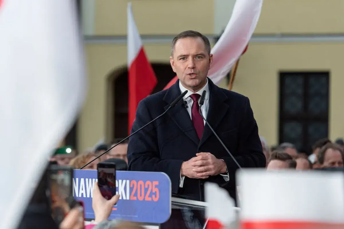 Polityk przemawia na tle flag. Na banerze widnieje napis "NAWROCKI 2025".