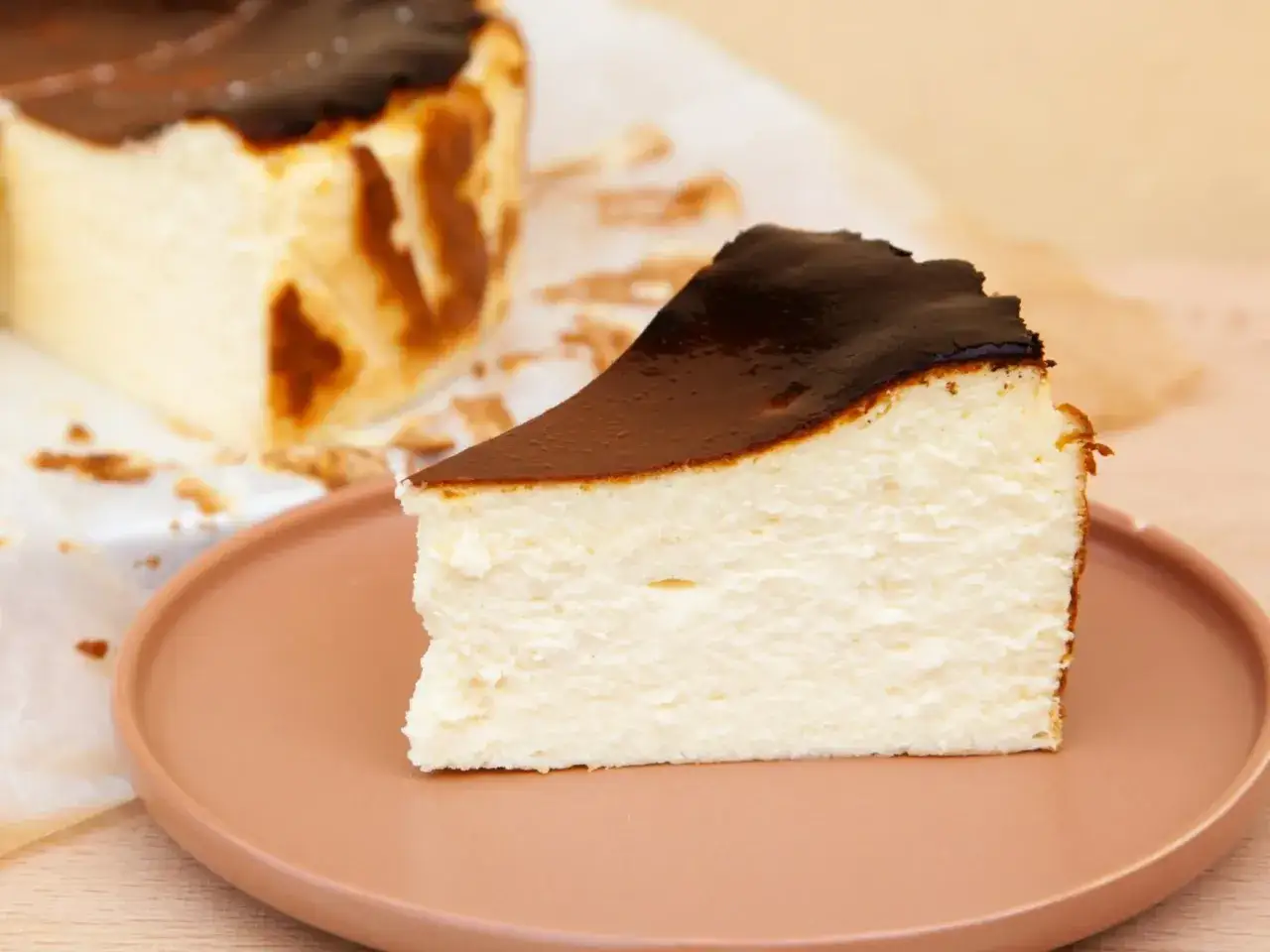 Kawałek kremowego sernika z przypaloną górą na różowym talerzu.