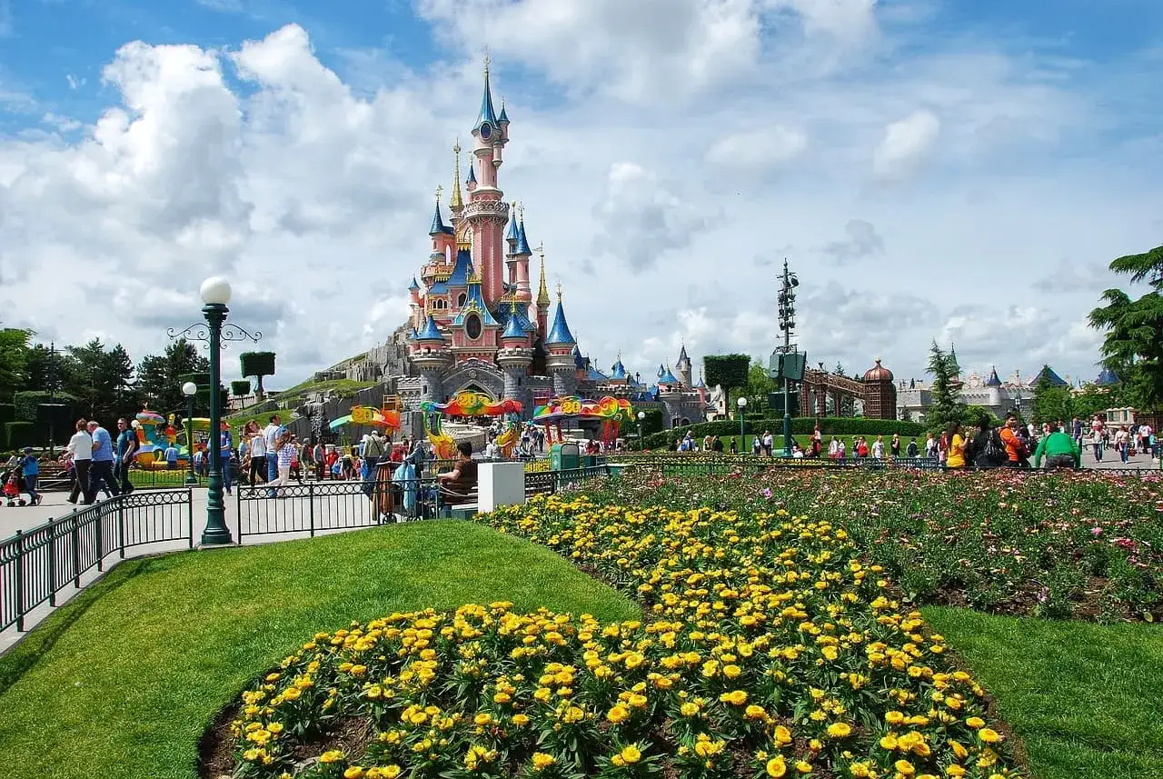 Disneyland Paris castle with colorful flowers and crowds of people.